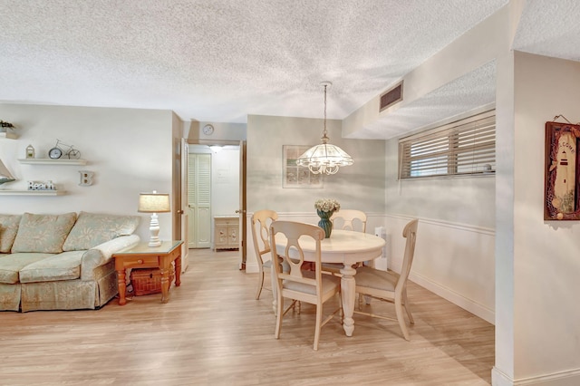 dining room with an inviting chandelier, a textured ceiling, and light wood-type flooring