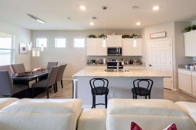 kitchen featuring appliances with stainless steel finishes, white cabinetry, sink, hanging light fixtures, and a center island with sink