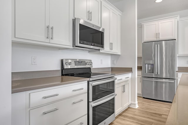 kitchen with appliances with stainless steel finishes, white cabinets, and light wood-type flooring