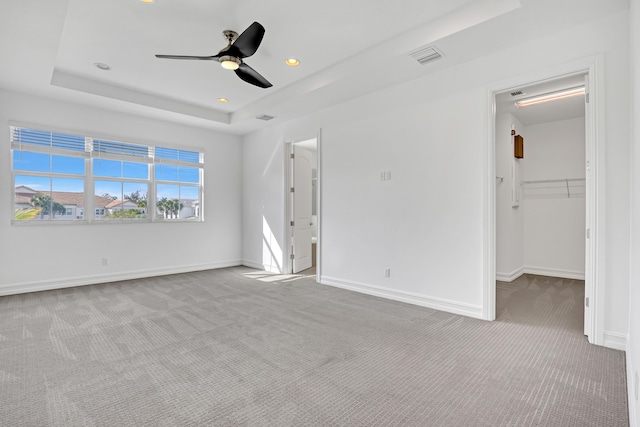 unfurnished bedroom with ceiling fan, a spacious closet, a raised ceiling, and light carpet