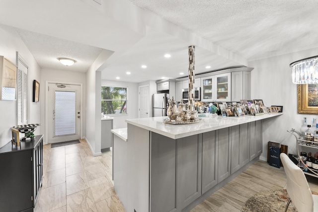 kitchen with gray cabinetry, kitchen peninsula, stainless steel appliances, light stone countertops, and a textured ceiling