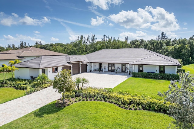 single story home with an attached garage, a tile roof, a front lawn, and decorative driveway