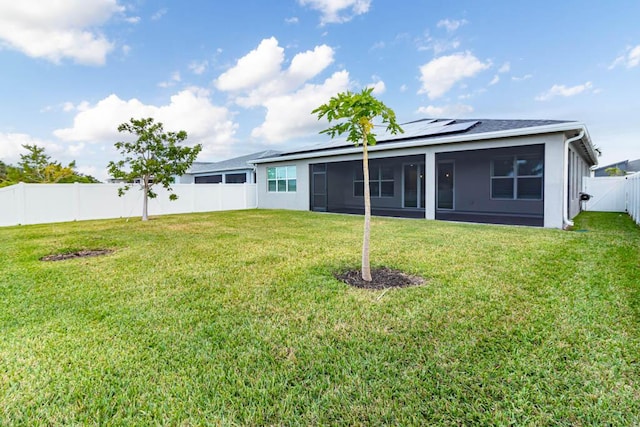 rear view of property featuring a lawn, a sunroom, and solar panels