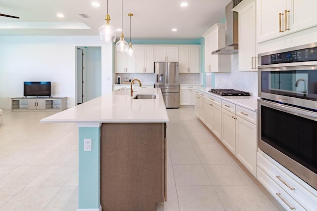 kitchen with appliances with stainless steel finishes, white cabinetry, hanging light fixtures, a center island with sink, and wall chimney exhaust hood