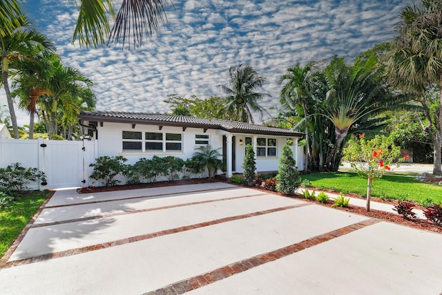 view of front facade with stucco siding, a front yard, fence, a tile roof, and a gate