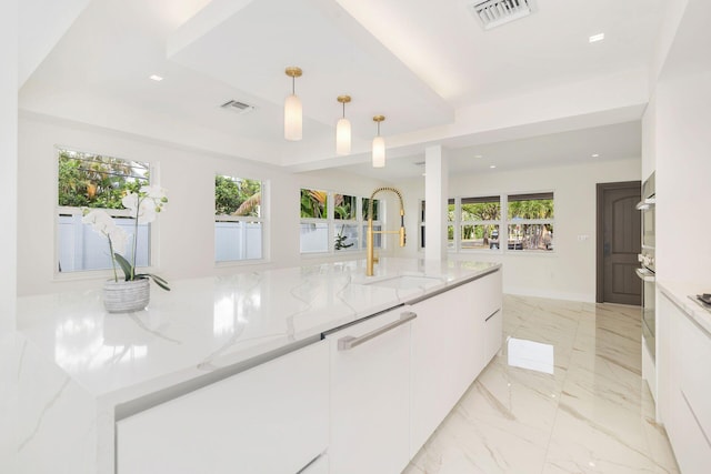 kitchen featuring hanging light fixtures, visible vents, white cabinets, and a sink