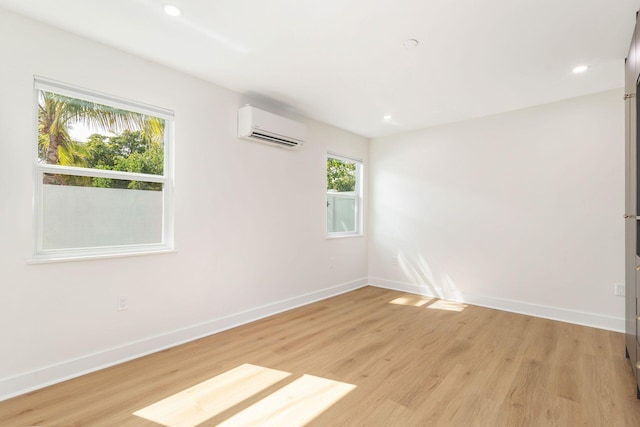 empty room featuring a wall mounted air conditioner, light wood finished floors, and baseboards