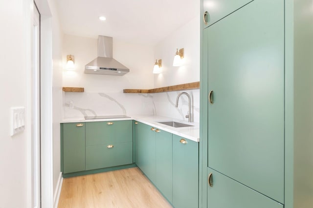 kitchen featuring green cabinets, wall chimney range hood, light wood-style flooring, backsplash, and a sink