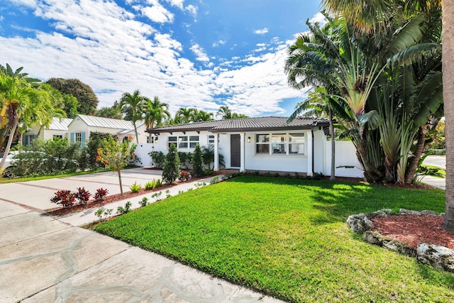 ranch-style house featuring concrete driveway, a front yard, a tiled roof, and stucco siding