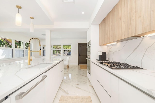 kitchen with modern cabinets, appliances with stainless steel finishes, marble finish floor, light stone counters, and decorative light fixtures