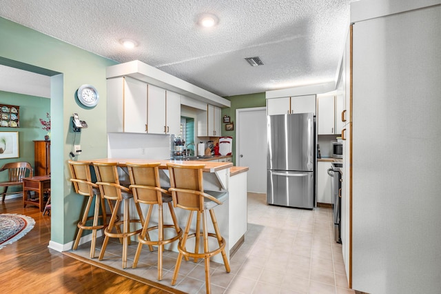 kitchen featuring sink, white cabinetry, a textured ceiling, stainless steel refrigerator, and a kitchen breakfast bar