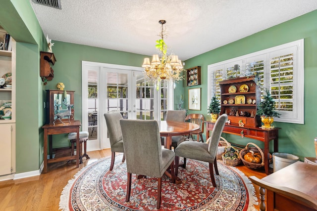 dining space featuring french doors, a healthy amount of sunlight, an inviting chandelier, and light hardwood / wood-style floors