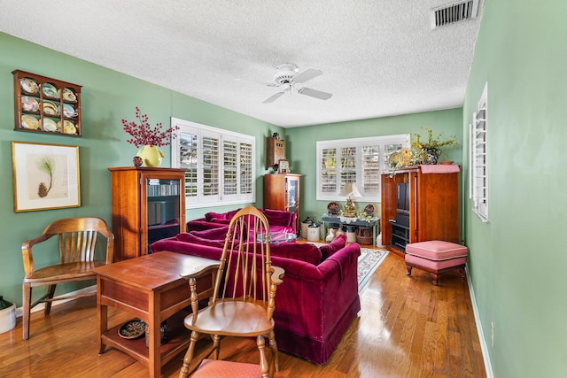 living room with hardwood / wood-style flooring, ceiling fan, and a textured ceiling