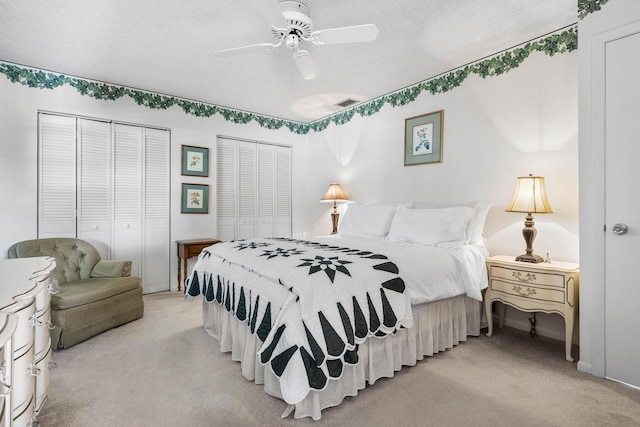 carpeted bedroom with ceiling fan, two closets, and a textured ceiling