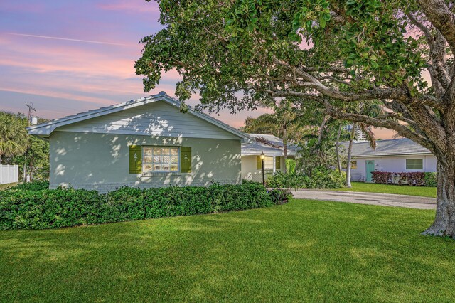 1210 Dolphin Rd, Singer Island, FL 33404 - back of property at dusk with fence, a lawn, a sunroom, and stucco siding