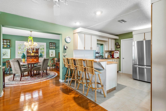 kitchen with stainless steel refrigerator, a breakfast bar area, white cabinets, hanging light fixtures, and kitchen peninsula