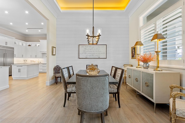 dining area with a chandelier, a tray ceiling, light wood finished floors, and a healthy amount of sunlight