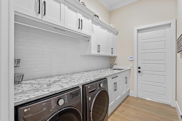 clothes washing area with cabinet space, baseboards, light wood-type flooring, separate washer and dryer, and a sink