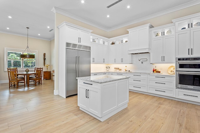 kitchen featuring light wood-style floors, ornamental molding, appliances with stainless steel finishes, backsplash, and a center island