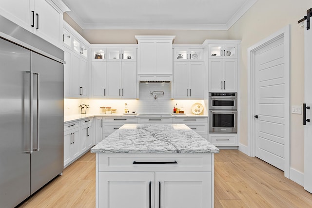 kitchen featuring light wood finished floors, stainless steel appliances, ornamental molding, and decorative backsplash