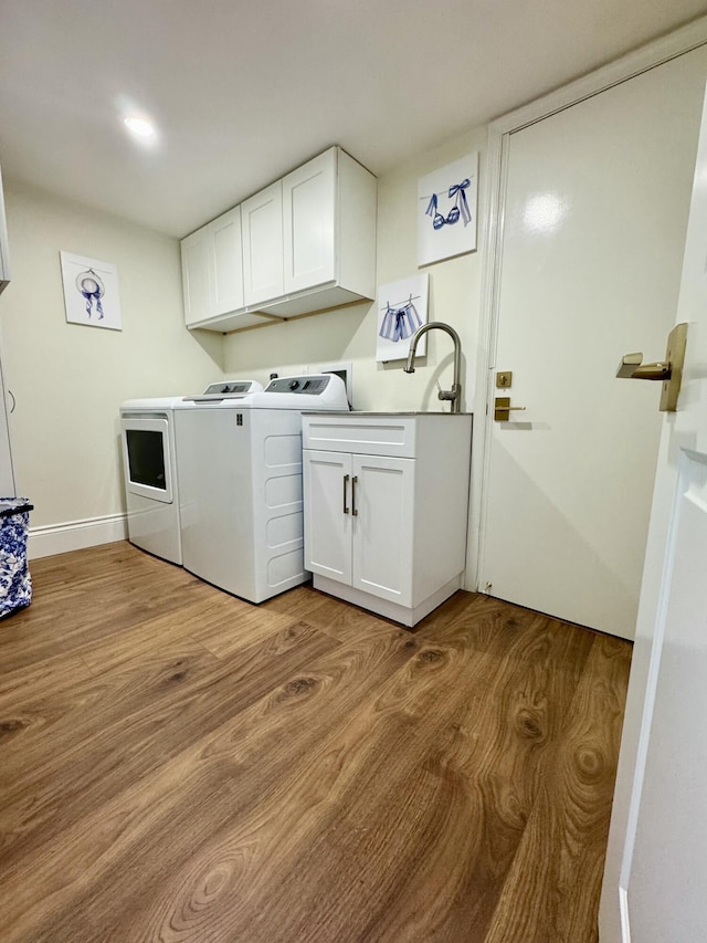 washroom with cabinets, washing machine and dryer, and light hardwood / wood-style floors