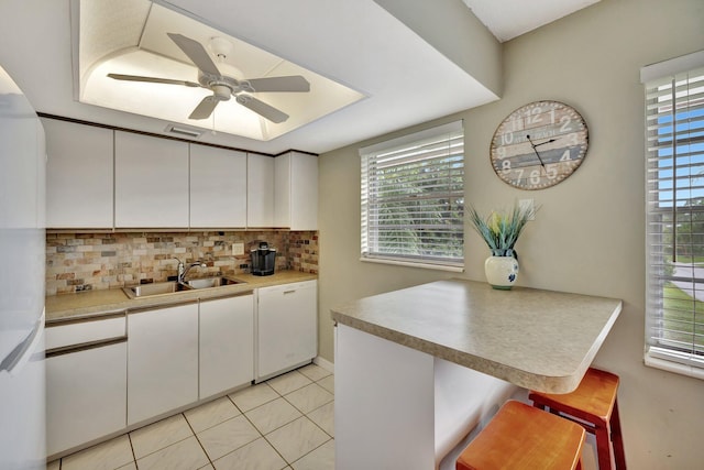 kitchen with white dishwasher, sink, a kitchen breakfast bar, and white cabinets