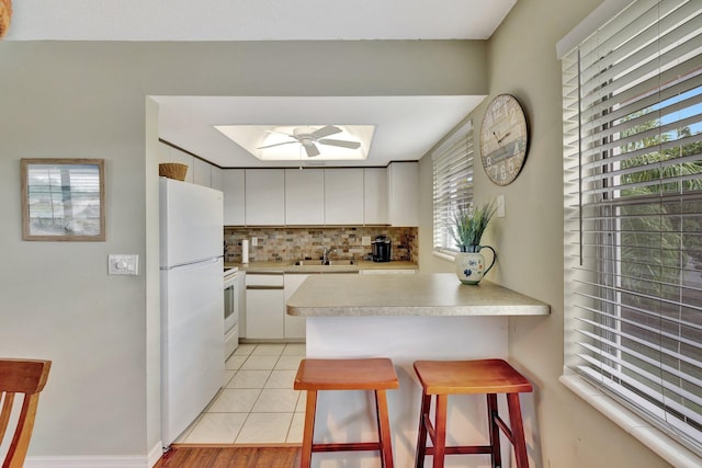 kitchen featuring white cabinetry, sink, a kitchen bar, kitchen peninsula, and white appliances