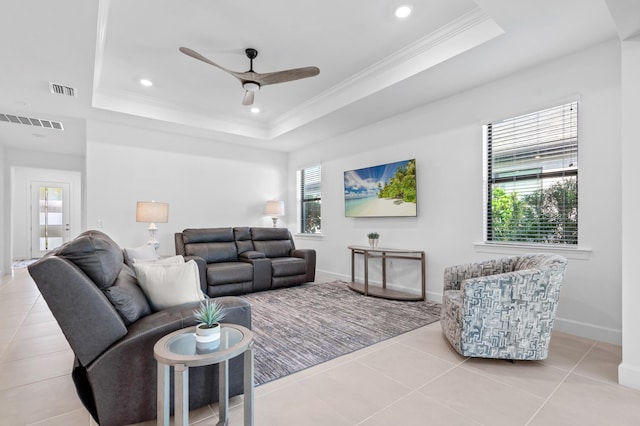 tiled living room with a raised ceiling, ornamental molding, and ceiling fan