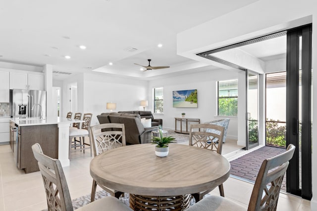 dining space with light tile patterned flooring, ceiling fan, and a tray ceiling