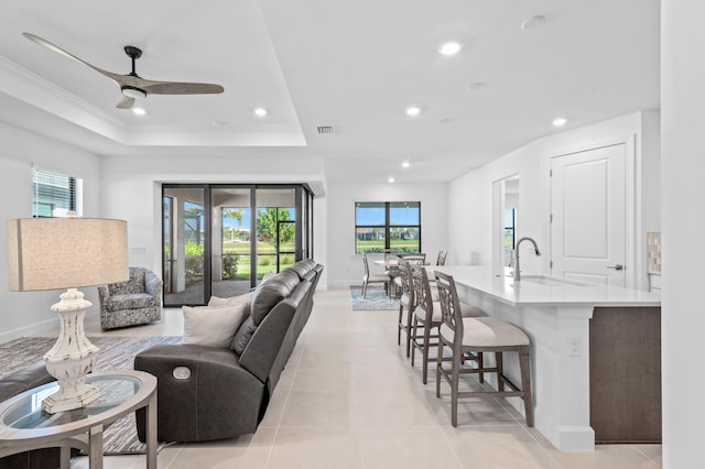 living room featuring sink, a tray ceiling, a wealth of natural light, and light tile patterned flooring