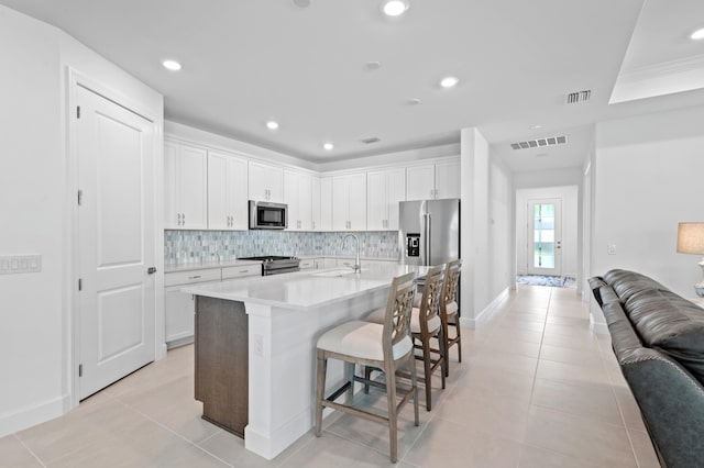 kitchen featuring sink, appliances with stainless steel finishes, a kitchen island with sink, white cabinets, and a kitchen bar