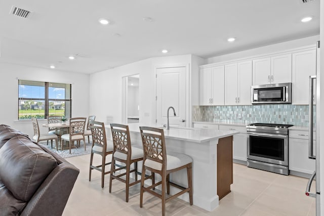 kitchen featuring white cabinetry, sink, backsplash, a kitchen island with sink, and stainless steel appliances