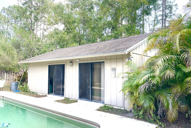 back of house featuring roof with shingles, an outdoor structure, and an outdoor pool