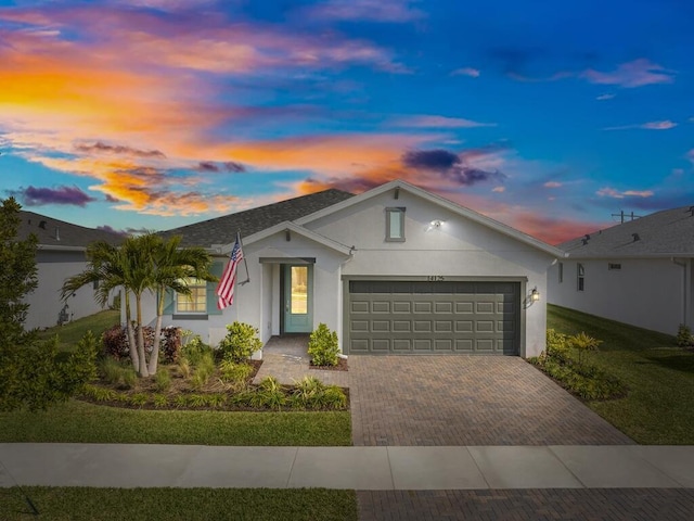 ranch-style house featuring decorative driveway, roof with shingles, an attached garage, and stucco siding