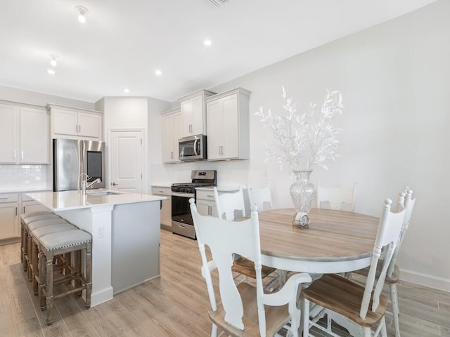 kitchen with stainless steel appliances, a sink, light wood-type flooring, tasteful backsplash, and an island with sink