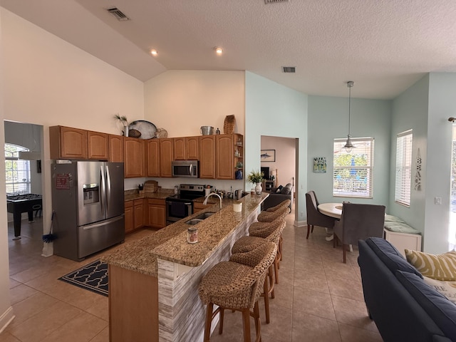 kitchen with stainless steel appliances, light stone countertops, light tile patterned flooring, decorative light fixtures, and kitchen peninsula