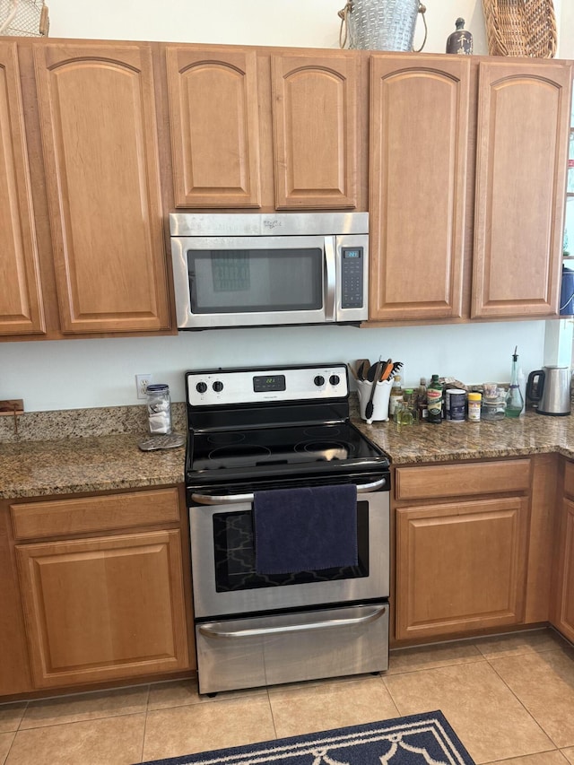 kitchen featuring appliances with stainless steel finishes, light tile patterned floors, and dark stone countertops