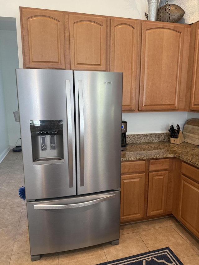 kitchen with dark stone countertops, light tile patterned floors, and stainless steel refrigerator with ice dispenser