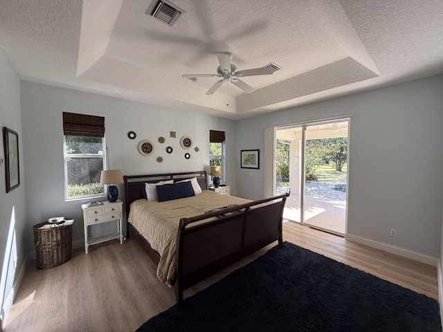 bedroom with access to exterior, a tray ceiling, wood-type flooring, and a textured ceiling