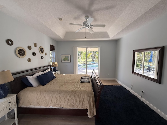 bedroom featuring ceiling fan, access to exterior, a raised ceiling, and a textured ceiling