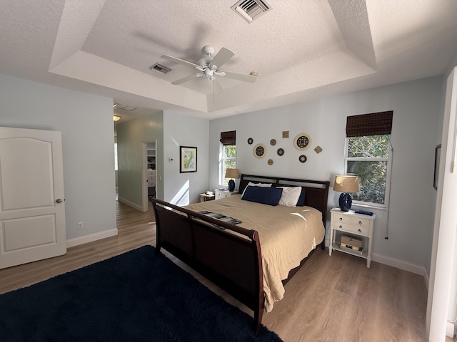 bedroom featuring ceiling fan, light hardwood / wood-style flooring, a textured ceiling, and a tray ceiling