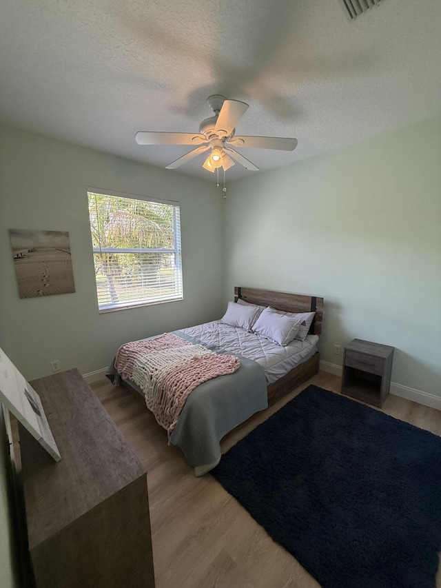 bedroom with hardwood / wood-style floors, a textured ceiling, and ceiling fan