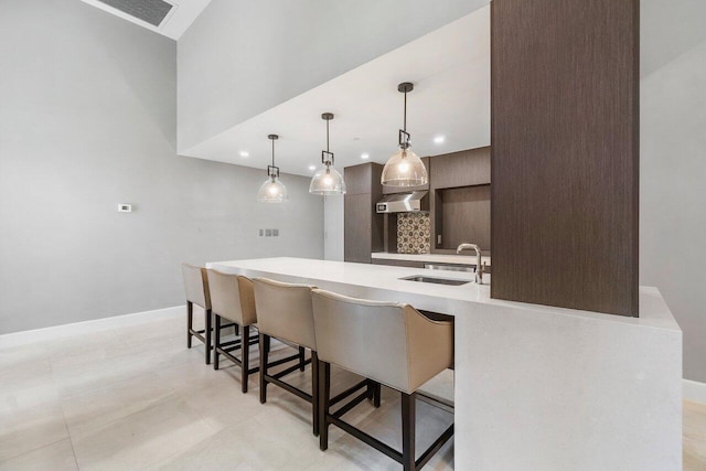 kitchen with dark brown cabinetry, a breakfast bar area, sink, and hanging light fixtures