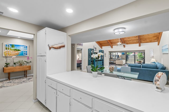 kitchen with wood ceiling, vaulted ceiling with skylight, white cabinets, and light tile patterned flooring