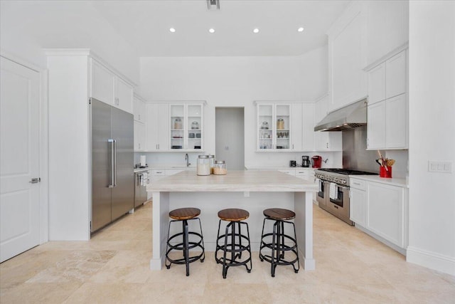 kitchen featuring a breakfast bar, white cabinetry, a towering ceiling, high quality appliances, and a kitchen island