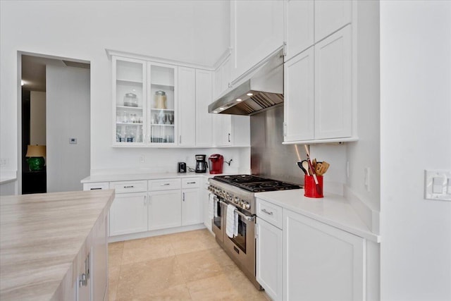 kitchen with range with two ovens, light tile patterned flooring, white cabinets, and wall chimney exhaust hood