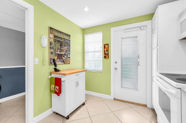 kitchen with white cabinetry, light tile patterned floors, white appliances, and wood counters