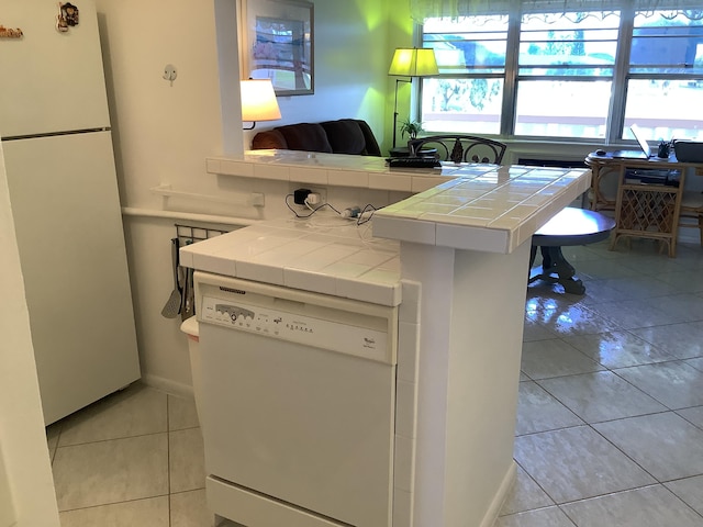 kitchen with tile countertops, light tile patterned flooring, a peninsula, white appliances, and white cabinetry