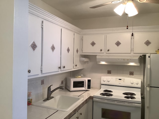 kitchen with white appliances, white cabinets, light countertops, under cabinet range hood, and a sink