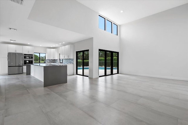 kitchen with a kitchen island, appliances with stainless steel finishes, a towering ceiling, white cabinetry, and backsplash